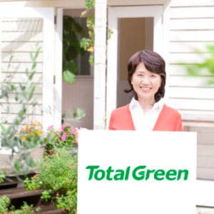 TotalGreenのロゴを掲げる主婦と明るい庭